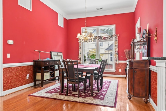 dining area with a wainscoted wall, ornamental molding, wood finished floors, and an inviting chandelier