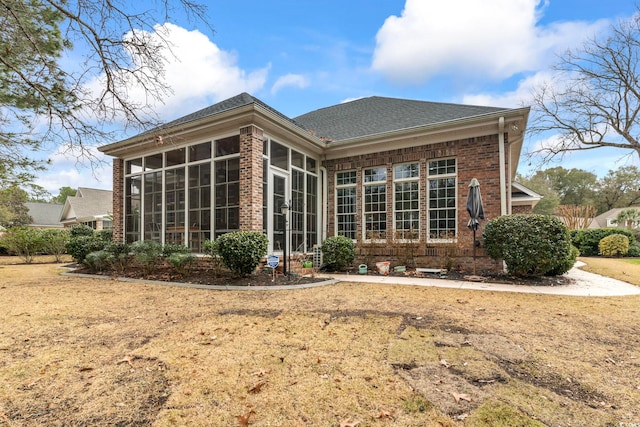 back of house featuring a sunroom, brick siding, and roof with shingles