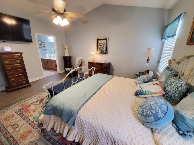 bedroom featuring baseboards, a ceiling fan, wood finished floors, ensuite bathroom, and vaulted ceiling