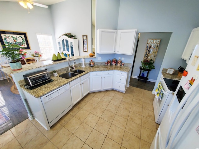 kitchen featuring a peninsula, white appliances, a high ceiling, a sink, and white cabinets