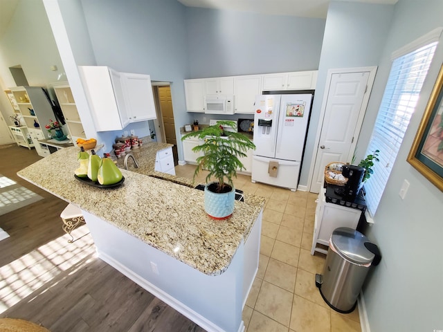 kitchen featuring white cabinetry, high vaulted ceiling, white appliances, a peninsula, and a kitchen breakfast bar