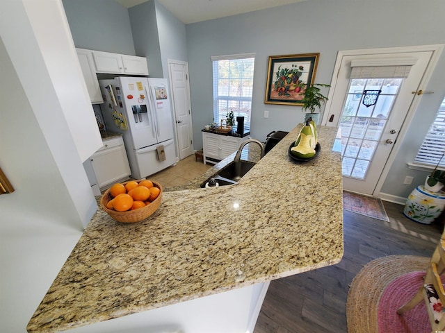 kitchen featuring white refrigerator with ice dispenser, dark wood finished floors, light stone counters, white cabinetry, and a sink