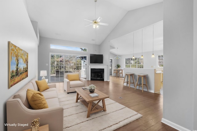 living room featuring baseboards, a ceiling fan, wood finished floors, a fireplace, and high vaulted ceiling