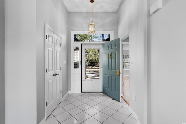 foyer entrance featuring an inviting chandelier, baseboards, light tile patterned floors, and a high ceiling