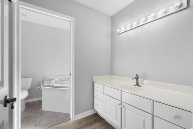 full bath featuring toilet, a garden tub, vanity, and baseboards