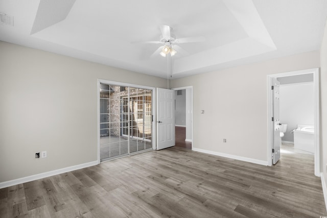 unfurnished room with a ceiling fan, baseboards, a tray ceiling, and wood finished floors