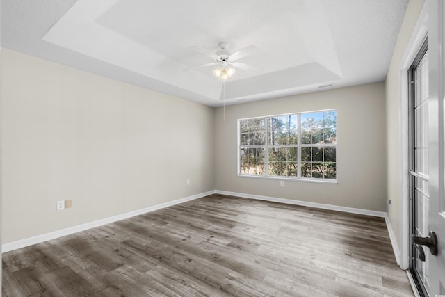 unfurnished bedroom featuring a tray ceiling, ceiling fan, baseboards, and wood finished floors