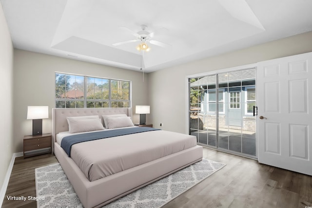 bedroom featuring access to outside, multiple windows, a raised ceiling, and wood finished floors