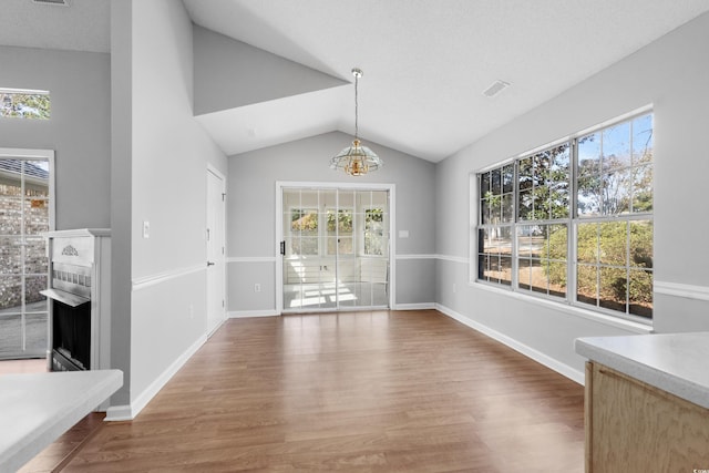 unfurnished dining area featuring lofted ceiling, a fireplace, baseboards, and wood finished floors