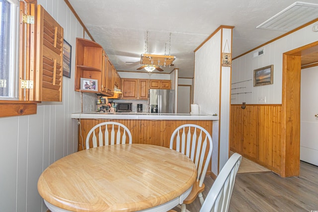 dining space with wood walls, visible vents, ornamental molding, and wood finished floors