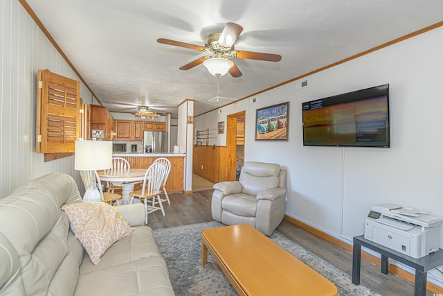 living area featuring a ceiling fan, visible vents, ornamental molding, and wood finished floors