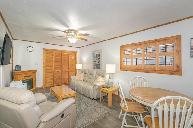 living area with ornamental molding, dark wood-type flooring, and a ceiling fan