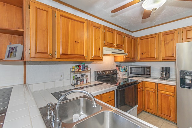 kitchen with under cabinet range hood, appliances with stainless steel finishes, brown cabinetry, and tile counters