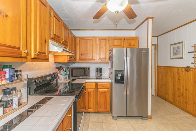 kitchen with brown cabinetry, tile countertops, appliances with stainless steel finishes, ornamental molding, and under cabinet range hood