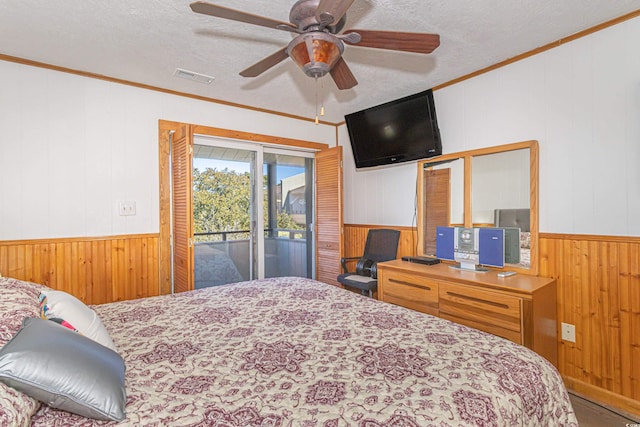 bedroom featuring a textured ceiling, wooden walls, visible vents, access to outside, and crown molding