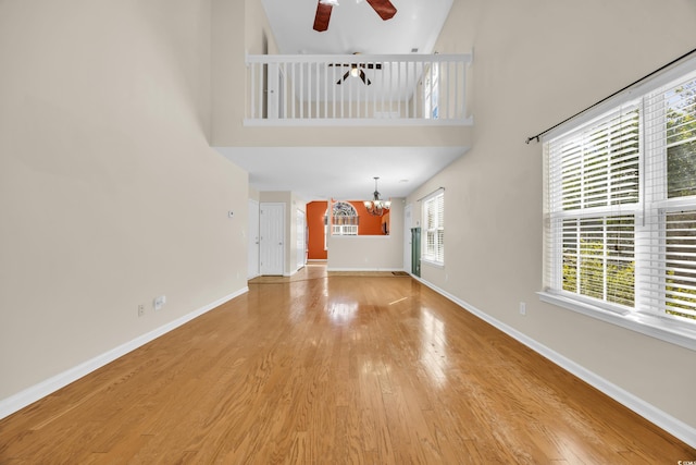 unfurnished living room with ceiling fan with notable chandelier, light wood finished floors, a high ceiling, and baseboards