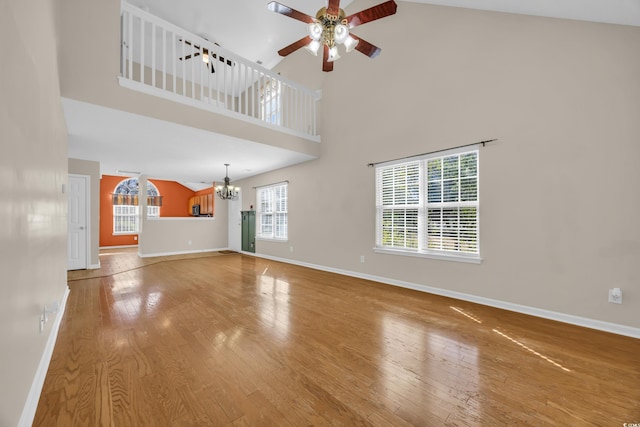 unfurnished living room featuring ceiling fan with notable chandelier, plenty of natural light, and wood finished floors