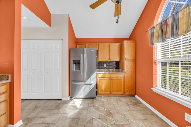 kitchen featuring lofted ceiling, backsplash, stone finish floor, stainless steel fridge, and baseboards