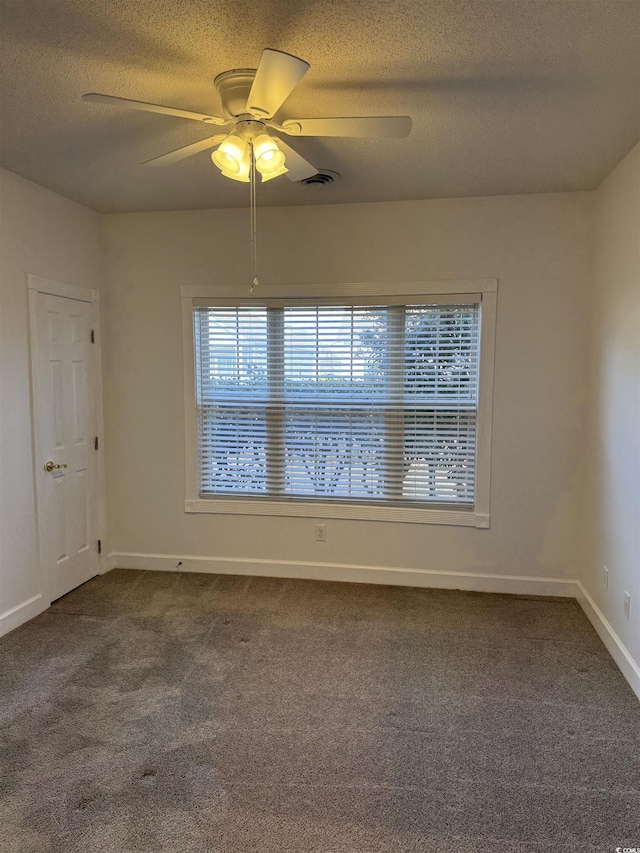 empty room with a textured ceiling, dark carpet, a ceiling fan, and baseboards