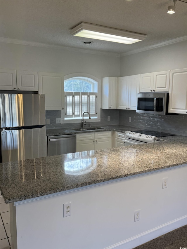 kitchen with stainless steel appliances, backsplash, white cabinetry, a sink, and dark stone counters