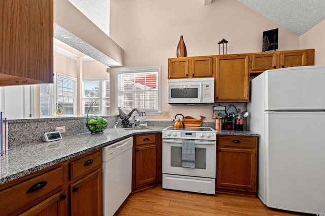 kitchen with light wood-type flooring, white appliances, brown cabinets, and a sink