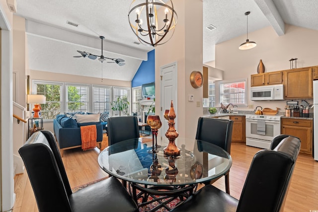 dining room featuring a textured ceiling, ceiling fan with notable chandelier, visible vents, light wood finished floors, and beamed ceiling