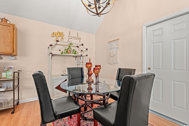 dining room with a textured ceiling, a chandelier, light wood-style flooring, baseboards, and vaulted ceiling