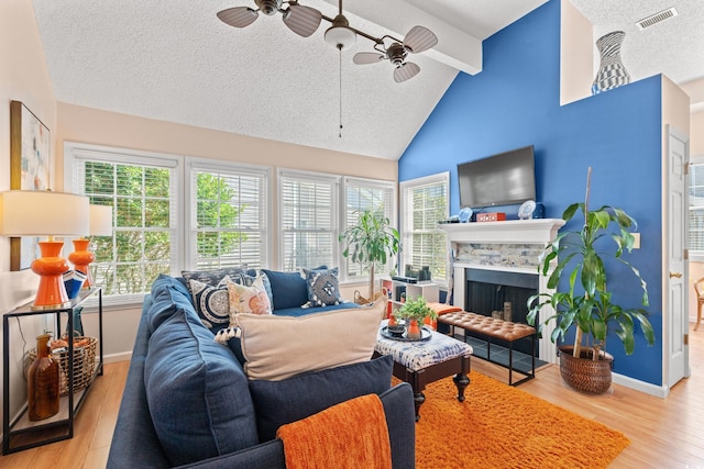 living area featuring a textured ceiling, a fireplace, visible vents, baseboards, and light wood finished floors