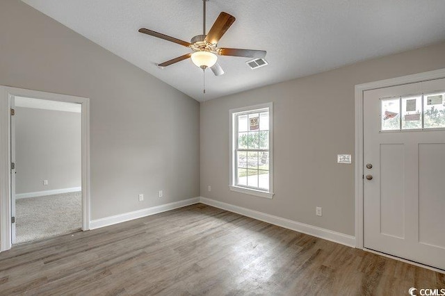 foyer entrance with lofted ceiling, visible vents, ceiling fan, wood finished floors, and baseboards