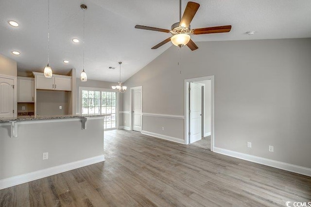 kitchen featuring wood finished floors, white cabinets, vaulted ceiling, a kitchen breakfast bar, and light stone countertops