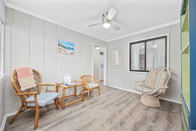 sitting room featuring a textured ceiling, light wood finished floors, a ceiling fan, and crown molding