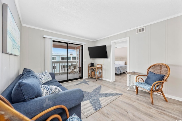 living room featuring a decorative wall, light wood-type flooring, visible vents, and crown molding