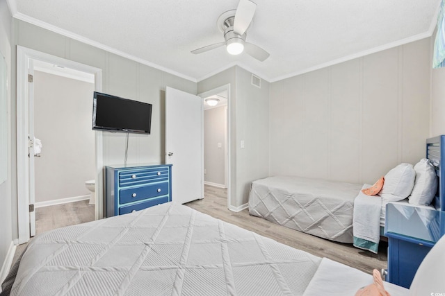 bedroom with light wood-style floors, visible vents, crown molding, and a decorative wall