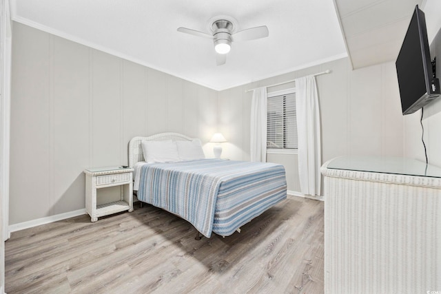 bedroom featuring ceiling fan, ornamental molding, light wood-type flooring, and a decorative wall