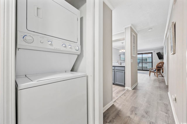 laundry area with stacked washer / drying machine, light wood-style floors, ornamental molding, laundry area, and baseboards