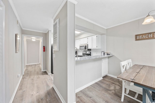 kitchen with light wood-style flooring, white cabinetry, stainless steel appliances, and ornamental molding