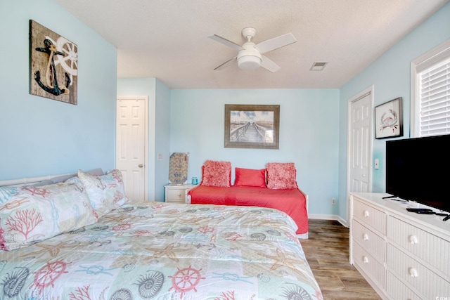 bedroom with visible vents, baseboards, light wood-type flooring, a textured ceiling, and a ceiling fan