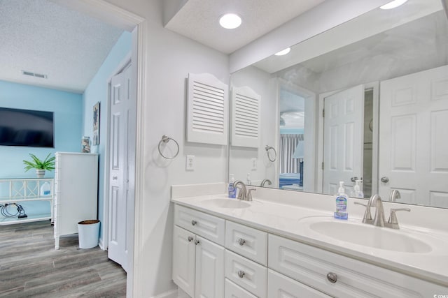 full bath featuring a textured ceiling, wood finished floors, visible vents, and a sink