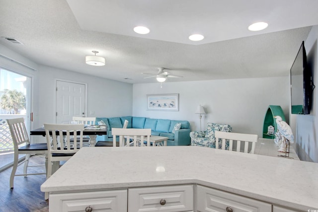 kitchen featuring visible vents, white cabinetry, light stone counters, a textured ceiling, and a ceiling fan