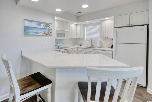 kitchen with visible vents, a peninsula, a kitchen breakfast bar, white appliances, and a sink