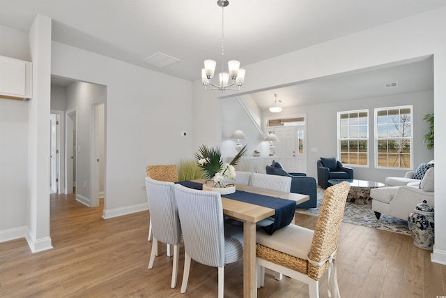 dining space with light wood finished floors, a notable chandelier, baseboards, and visible vents