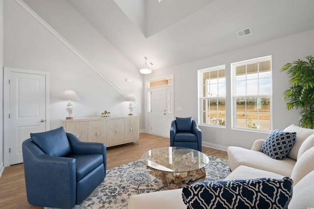living area with vaulted ceiling, visible vents, baseboards, and wood finished floors