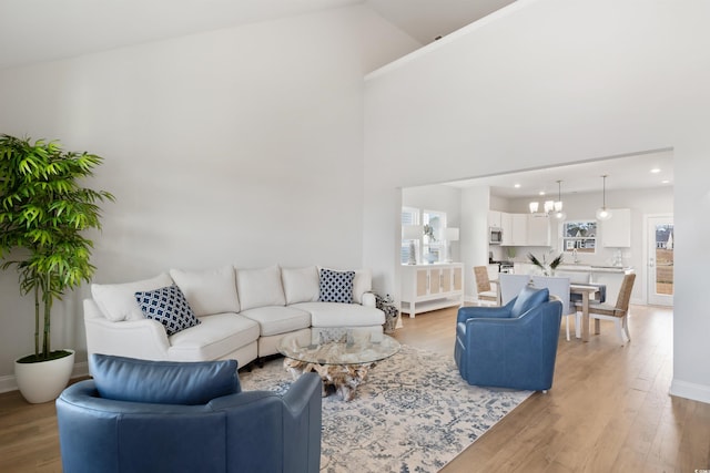 living area featuring an inviting chandelier, light wood-style floors, baseboards, and high vaulted ceiling
