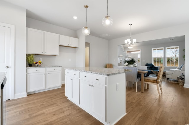 kitchen with pendant lighting, open floor plan, light wood-style floors, white cabinets, and light stone countertops
