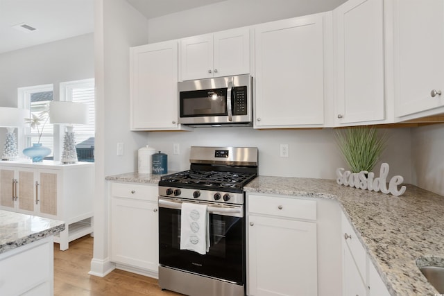 kitchen with light stone counters, visible vents, white cabinets, light wood-style floors, and appliances with stainless steel finishes