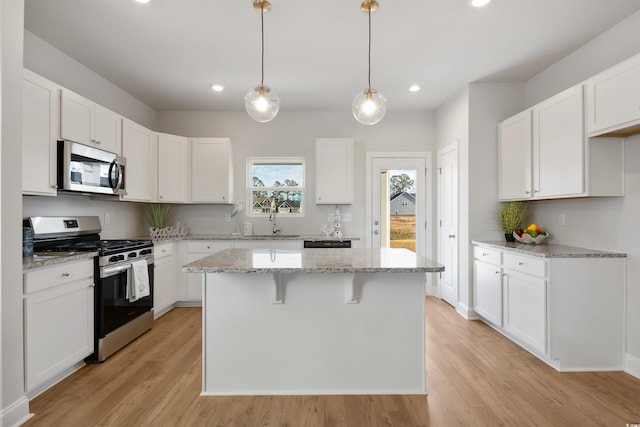 kitchen featuring a kitchen island, white cabinetry, stainless steel appliances, light wood-style floors, and light stone countertops