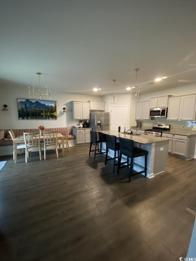 kitchen with pendant lighting, stainless steel appliances, dark wood-type flooring, a kitchen island with sink, and white cabinetry