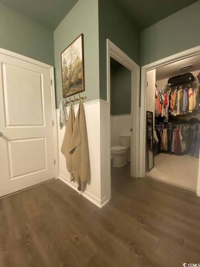 bathroom with a walk in closet, wainscoting, toilet, and wood finished floors