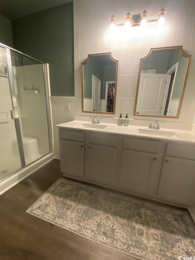 full bath with double vanity, a shower with shower door, a sink, and wood finished floors