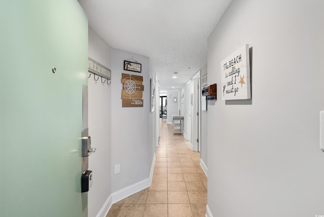 corridor featuring a textured ceiling, baseboards, and light tile patterned floors